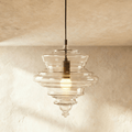 Clérachic's pendant light in clear glass, its tiered ribbed shade glowing warm on a slender dark cord.