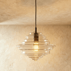A closer view of the Clérachic pendant light in clear glass, its tiered ribbed shade glowing warm overhead.