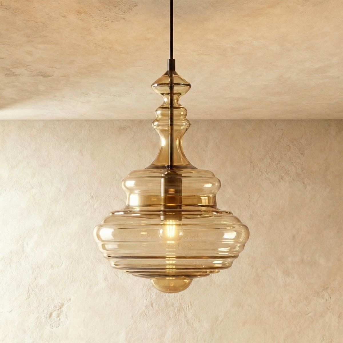Clérachic's pendant light in cognac glass, a tall fluted decanter-shaped shade glowing warm overhead.