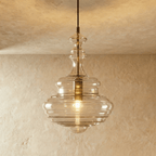 Clérachic's pendant light in clear glass, its tall fluted decanter-shaped shade glowing warm on a dark cord.