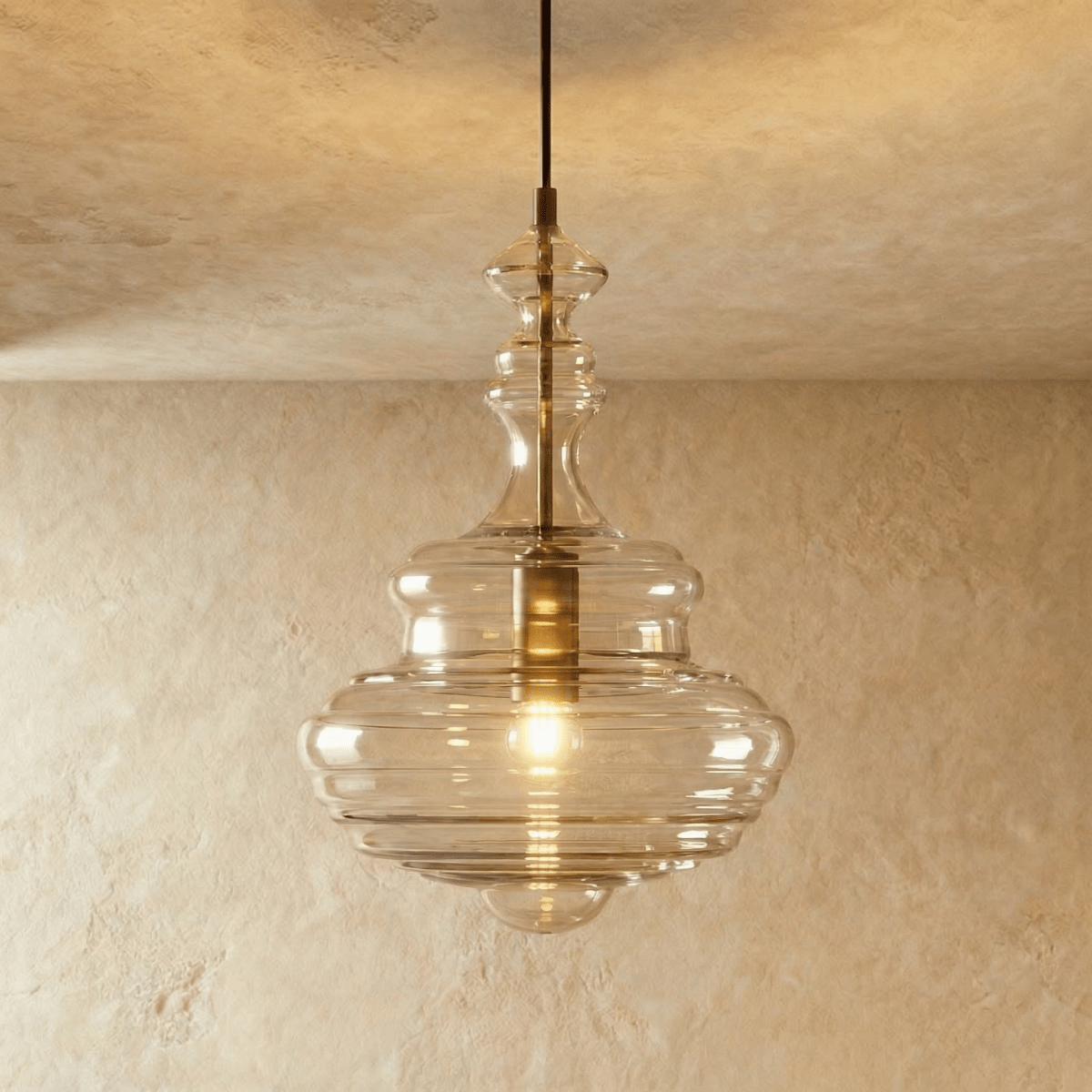 Clérachic's pendant light in clear glass, its tall fluted decanter-shaped shade glowing warm on a dark cord.