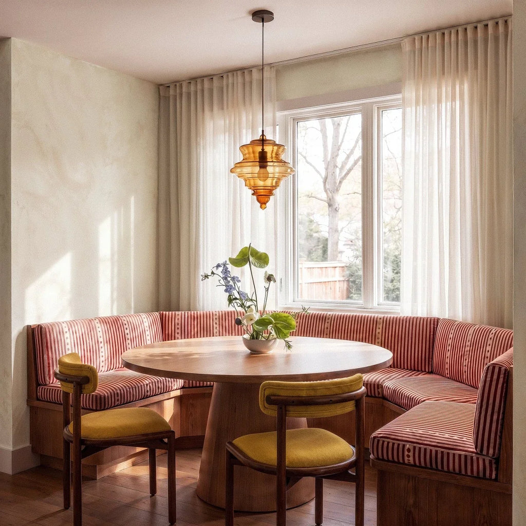 Clérachic's pendant light in cognac glass, hanging above a round dining table in a sunlit striped banquette.