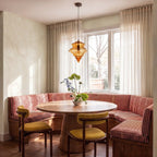 Clérachic's pendant light in cognac glass, hanging above a round dining table in a sunlit striped banquette.