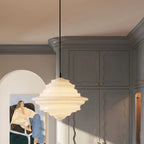 A closer view of the Clérachic pendant light in milk white glass, its tiered shade beside gray cabinetry.