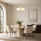 Above a round fluted dining table with cream chairs, a Clérachic chandelier hangs in a room with an arched window.