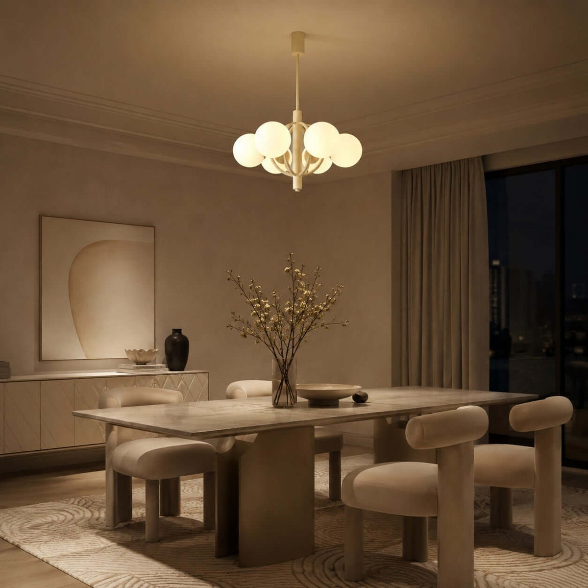 Lit warm in the evening, a Clérachic chandelier hangs over a stone dining table with rounded, cushioned chairs.