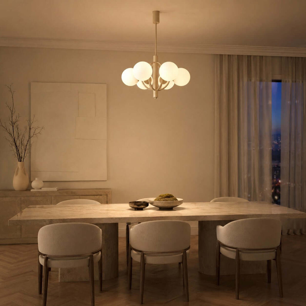 At night, a Clérachic chandelier glows over a long stone table with curved-back chairs and a sheer curtain at the window.