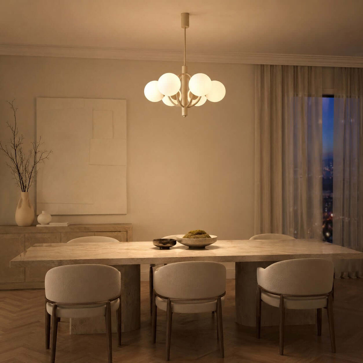 At night, a Clérachic chandelier glows over a long stone table with curved-back chairs and a sheer curtain at the window.