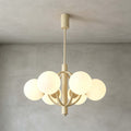 A Clérachic chandelier with milk-white globes and curved beige arms, lit and hung against a grey concrete wall.