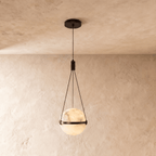 Clérachic alabaster globe pendant lit from within, held by three fine cords in a dark bronze band, on a limewash wall.
