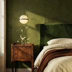Clérachic alabaster globe pendant lit beside a dark green velvet headboard above a carved wooden bedside table.