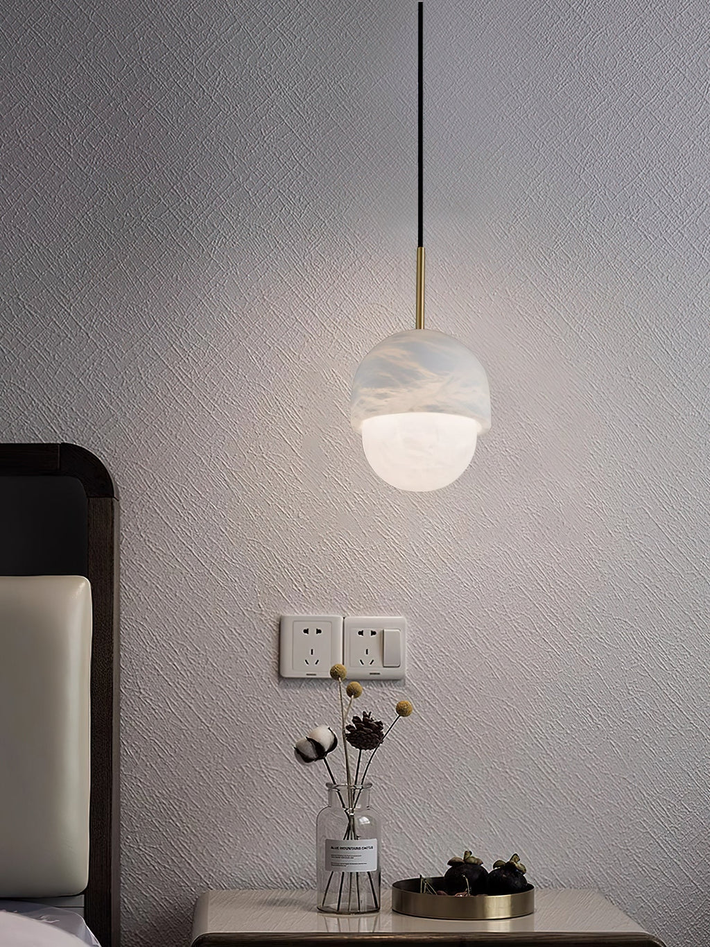 Clérachic Mini Alabaster Globe Pendant lit above a bedside table, pooling warm light on the wall behind it.