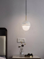 Clérachic Mini Alabaster Globe Pendant lit above a bedside table, pooling warm light on the wall behind it.