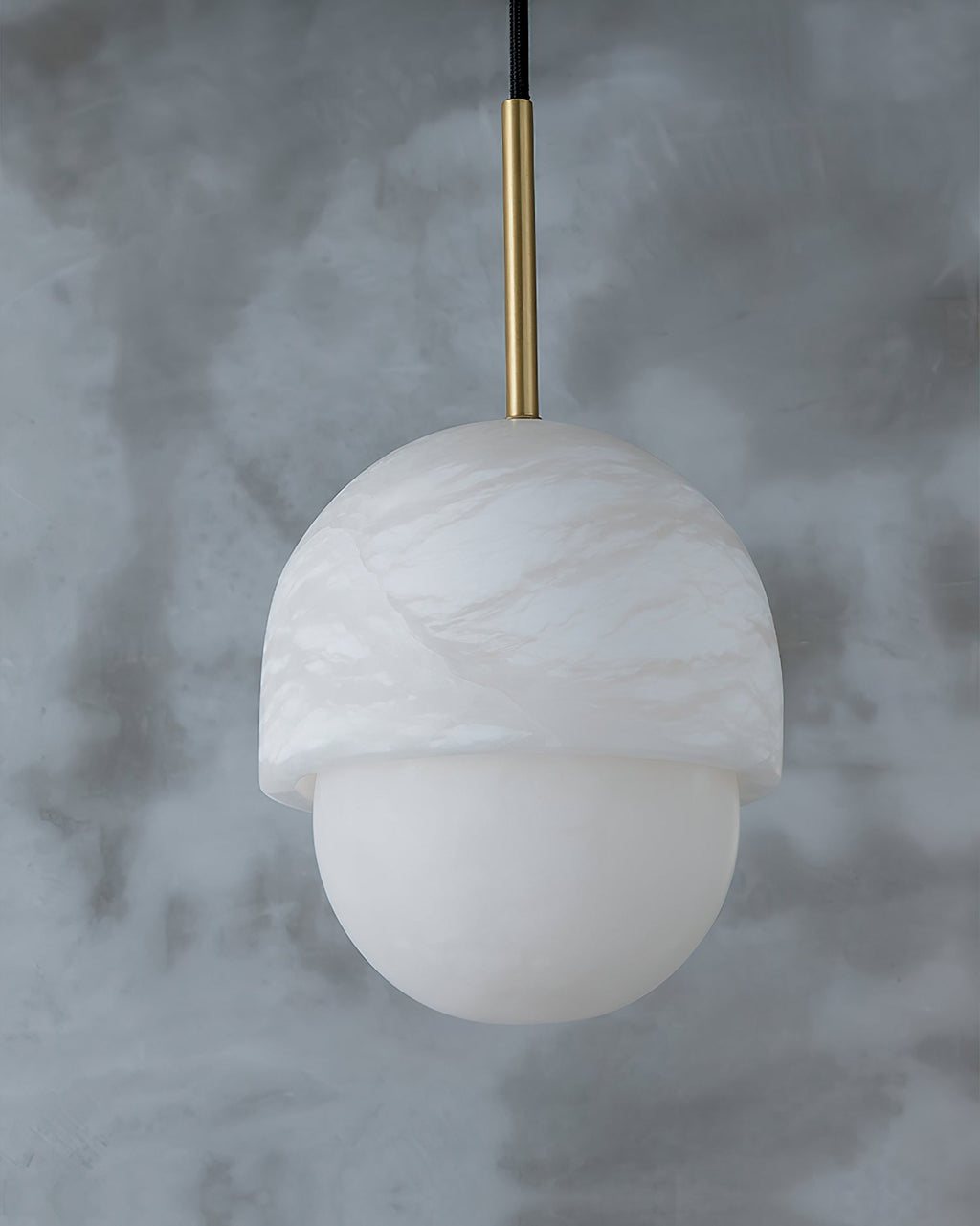 Studio view of the Clérachic Mini Alabaster Globe Pendant against grey plaster, its stone cap and lower globe clear.