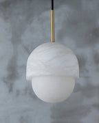 Studio view of the Clérachic Mini Alabaster Globe Pendant against grey plaster, its stone cap and lower globe clear.