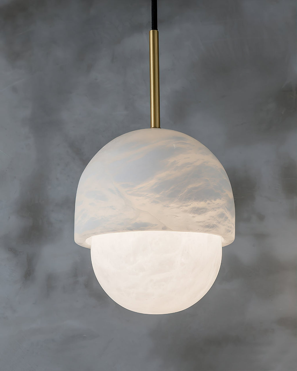 Clérachic Mini Alabaster Globe Pendant switched on, the stone cap warming through above the glowing lower sphere.