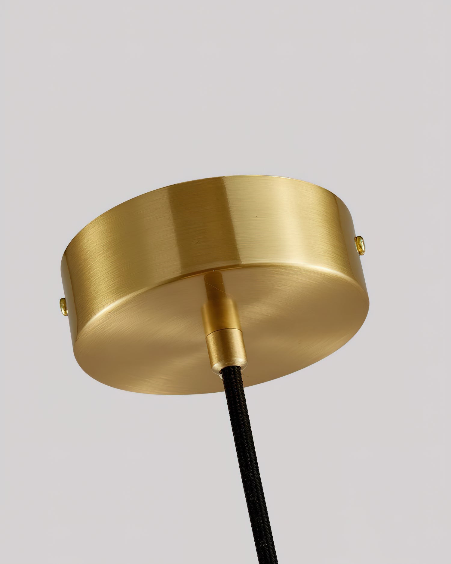 Brushed brass ceiling canopy of the Clérachic Mini Alabaster Globe Pendant, black fabric cord running from its centre.