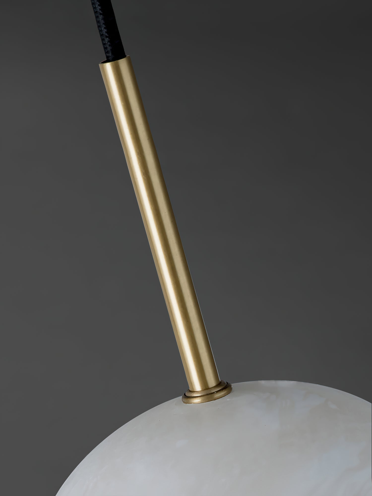 Slim brass stem meeting its collar on the Clérachic Mini Alabaster Globe Pendant, shot against a dark grey ground.