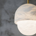Close crop of the lit Clérachic Mini Alabaster Globe Pendant, veining in the cap glowing above the bright lower globe.