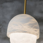 The Clérachic Mini Alabaster Globe Pendant lit from within, stone cap seated over the softly bright lower sphere.