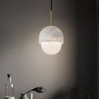 Clérachic Mini Alabaster Globe Pendant lit over a dark sideboard set with a glass bottle and a dried flower.