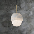 Clérachic Mini Alabaster Globe Pendant hung against mottled grey concrete, warm light spilling from the lower globe.