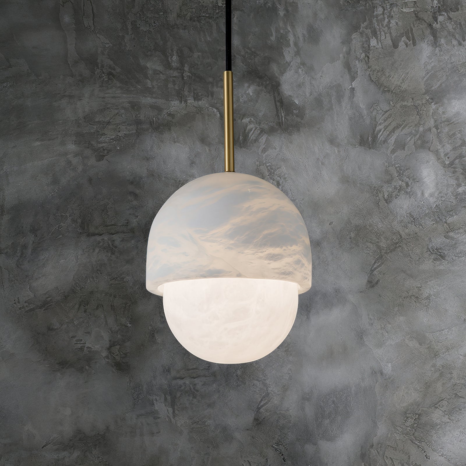 Clérachic Mini Alabaster Globe Pendant hung against mottled grey concrete, warm light spilling from the lower globe.