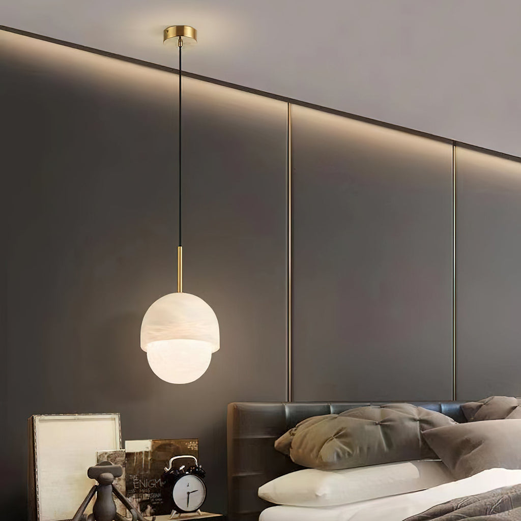 Clérachic Mini Alabaster Globe Pendant dropped on a long cord beside a bed, lit against a panelled bedroom wall.