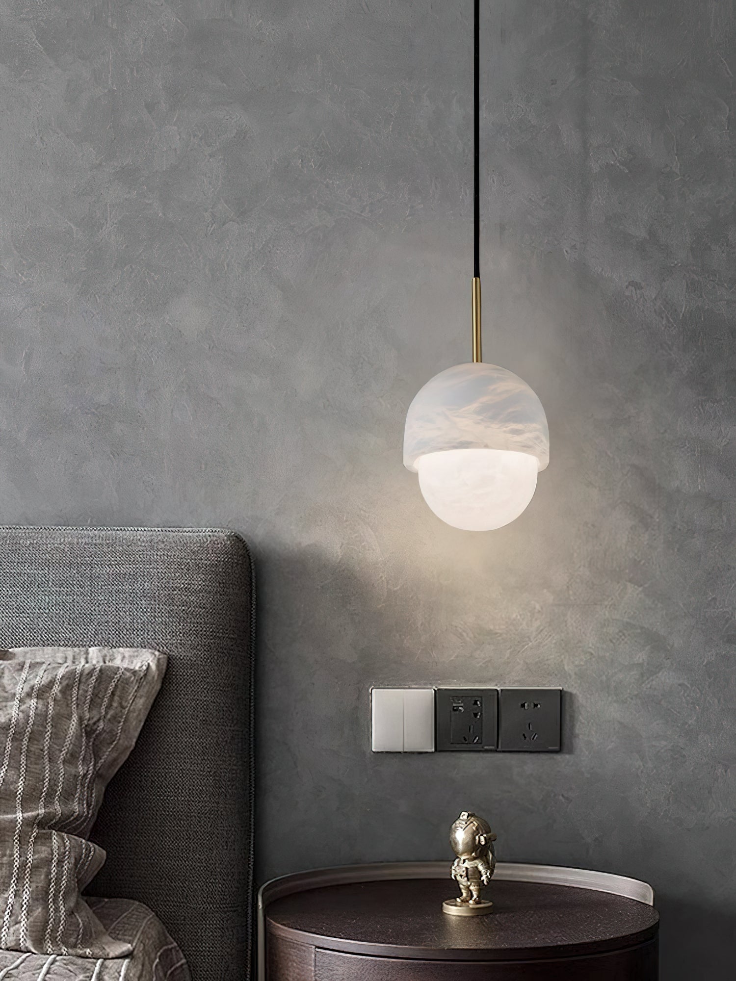 Clérachic Mini Alabaster Globe Pendant beside a grey upholstered headboard, lit above a round bedside table.