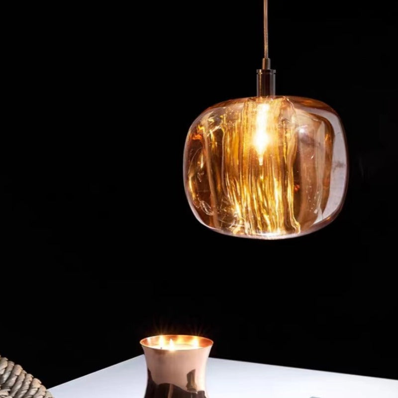 An amber Clérachic mini bubble glass pendant light lit against a dark backdrop, its internal striations flaring gold above a white table