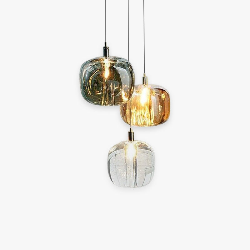 Staggered cluster of three Clérachic mini bubble glass pendant lights — smoky gray, amber and clear — lit on a plain studio backdrop