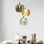 Three Clérachic mini bubble glass pendant lights clustered at staggered drops above a dining table laid with cheese and brass tins