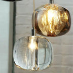 Close view of amber and clear Clérachic mini bubble glass pendant lights lit against a whitewashed brick wall