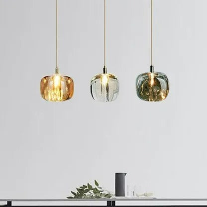 A row of three Clérachic mini bubble glass pendant lights in amber, clear and smoky gray, lit above a console with foliage