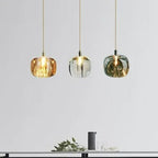 A row of three Clérachic mini bubble glass pendant lights in amber, clear and smoky gray, lit above a console with foliage