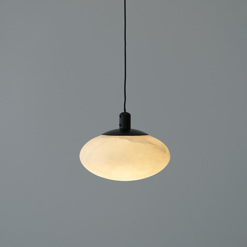 Clérachic Mini Discus pendant light unlit, its pale alabaster shade and matte black cap against a grey studio wall.