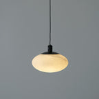 Clérachic Mini Discus pendant light unlit, its pale alabaster shade and matte black cap against a grey studio wall.