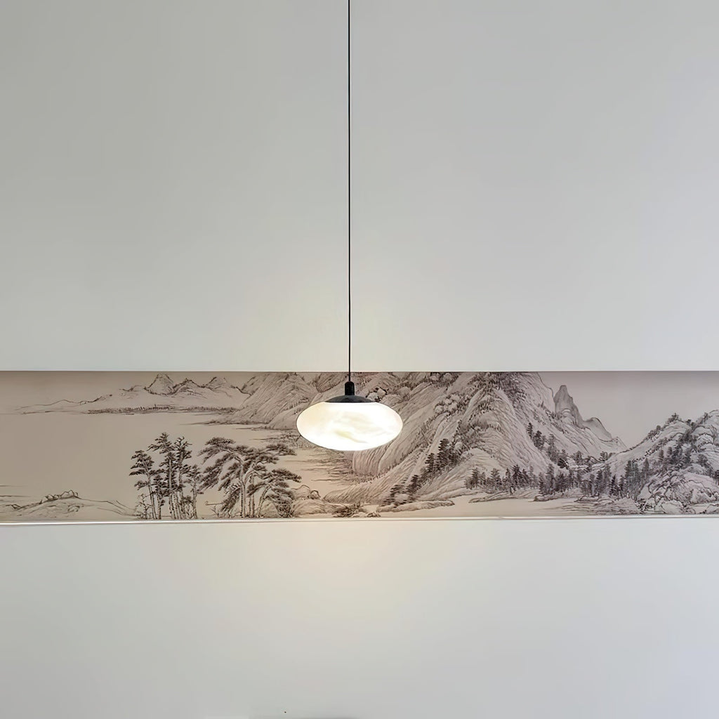 Clérachic Mini Discus pendant light hanging low over an ink-wash landscape panel, one small glowing accent in a wide room.