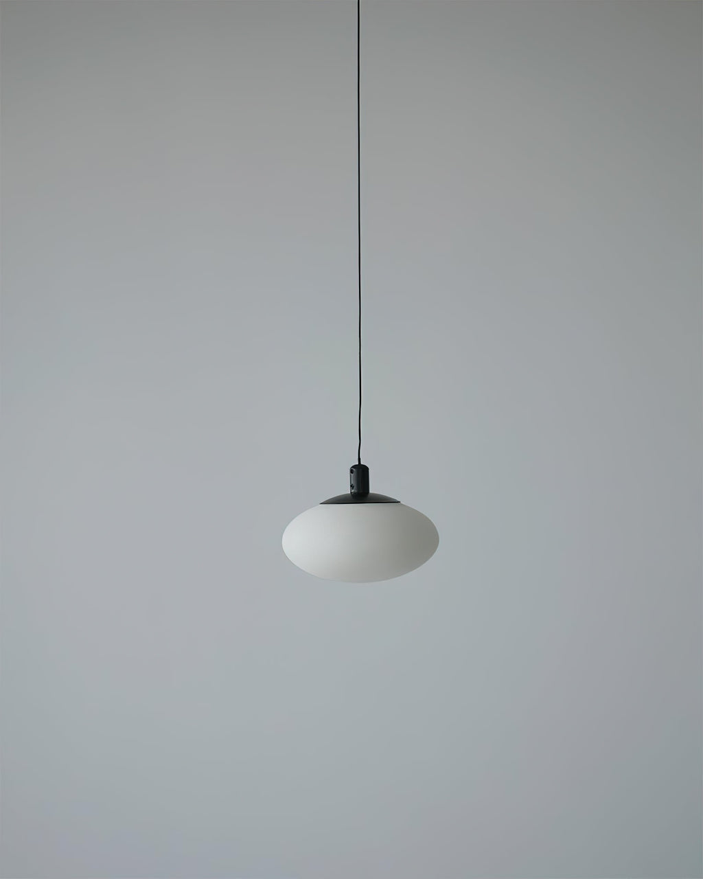 Unlit Clérachic Mini Discus pendant light on a pale grey wall, the alabaster reading as cool chalky stone from across the room.