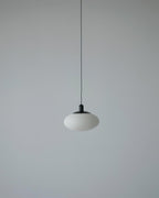 Unlit Clérachic Mini Discus pendant light on a pale grey wall, the alabaster reading as cool chalky stone from across the room.