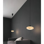 Two Clérachic Mini Discus pendant lights at staggered heights above a grey sofa, dished undersides glowing amber.
