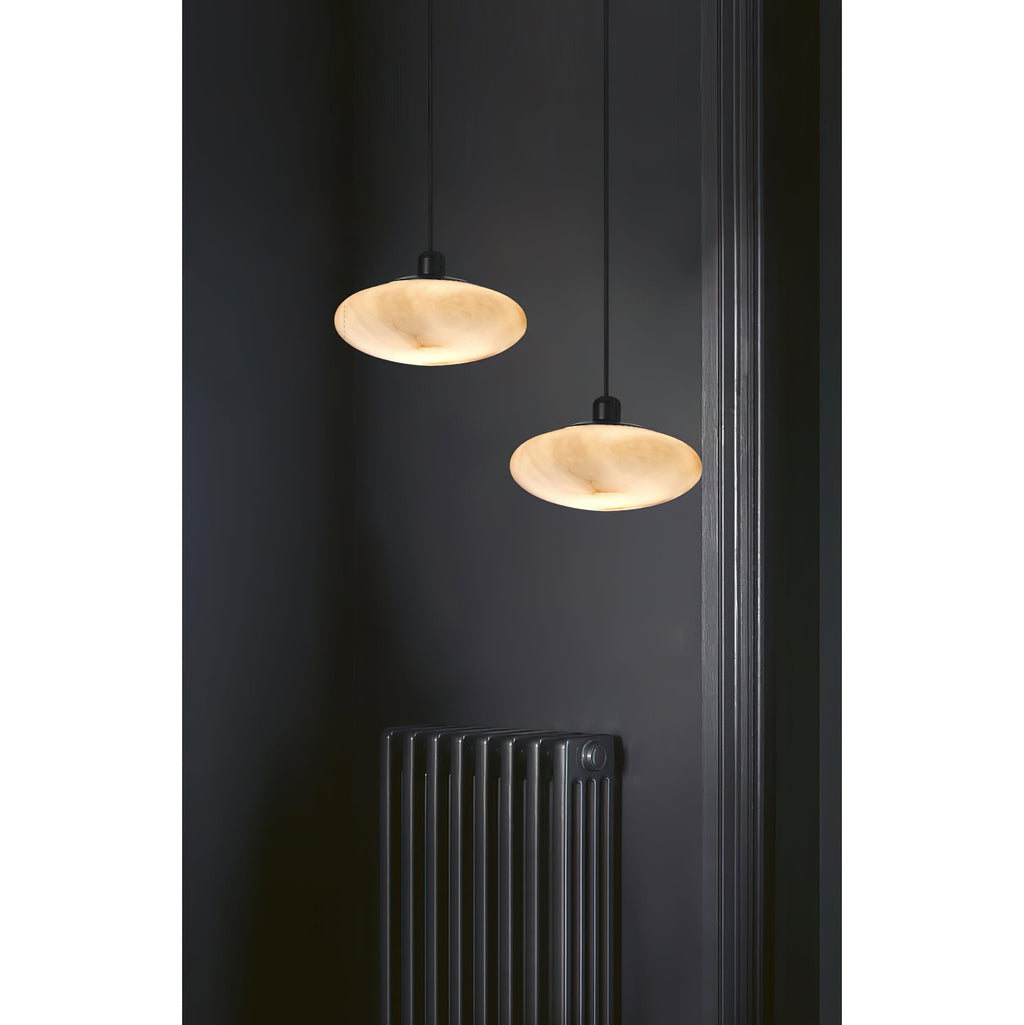 A pair of Clérachic Mini Discus pendant lights hung at different drops beside a column radiator on a near-black wall.