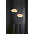 A pair of Clérachic Mini Discus pendant lights hung at different drops beside a column radiator on a near-black wall.