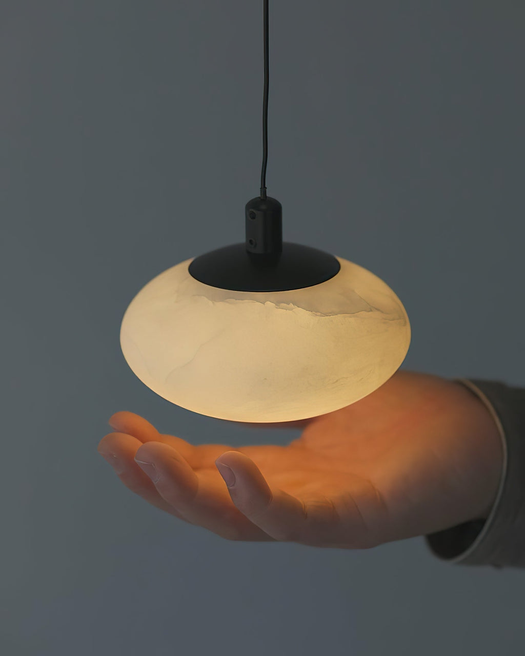 Clérachic Mini Discus pendant light held above an open palm, showing how the lit shade spans about a hand's width.
