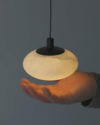Clérachic Mini Discus pendant light held above an open palm, showing how the lit shade spans about a hand's width.