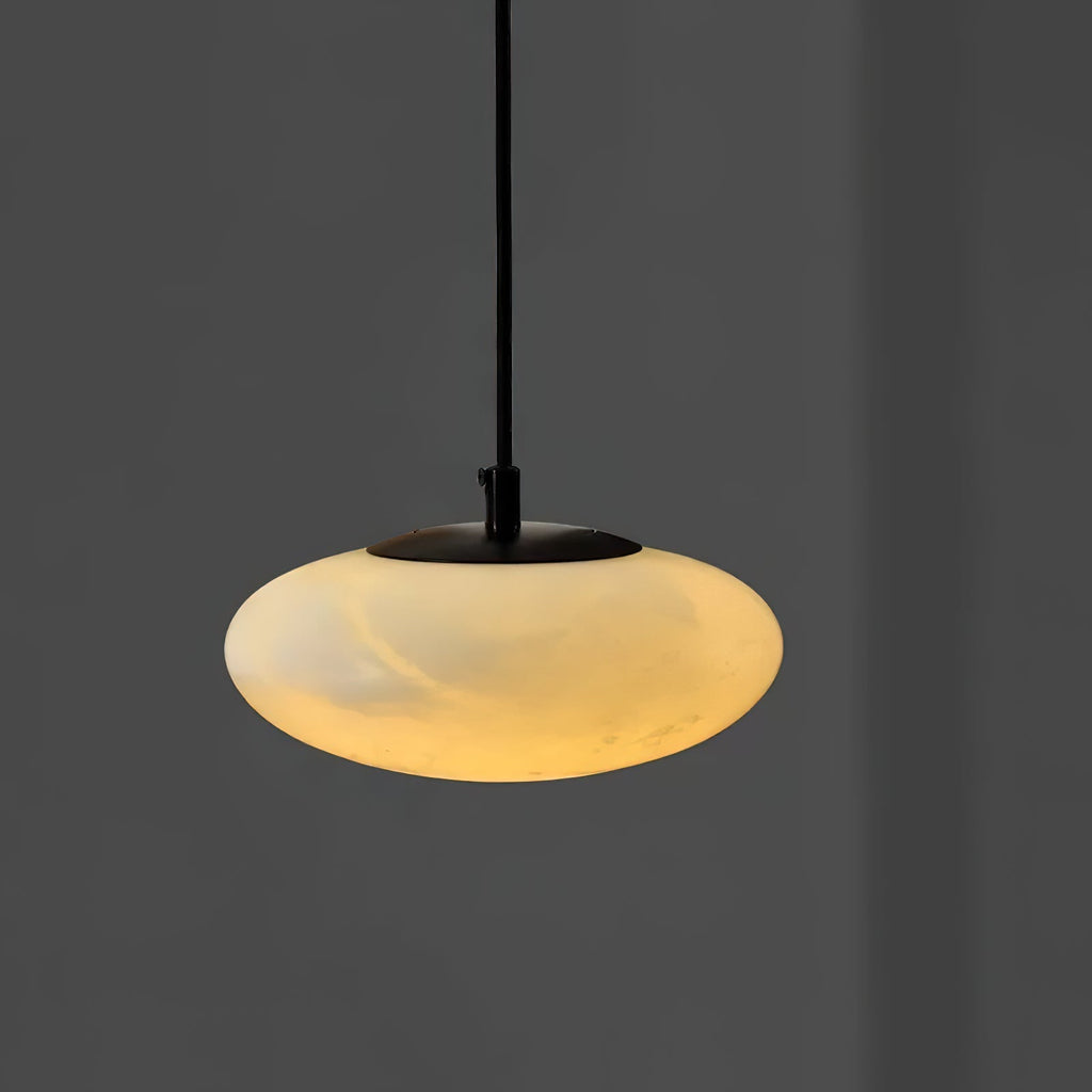 Close view of the Clérachic Mini Discus pendant light lit to deep honey, the black stem and cap sitting quietly above.