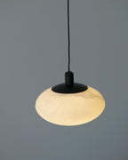 Clérachic Mini Discus pendant light glowing softly on a grey backdrop, cloudy veining just readable across the shade.
