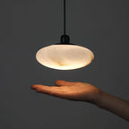 An open hand beneath the lit Clérachic Mini Discus pendant light, its dished underside casting warm light onto the palm.