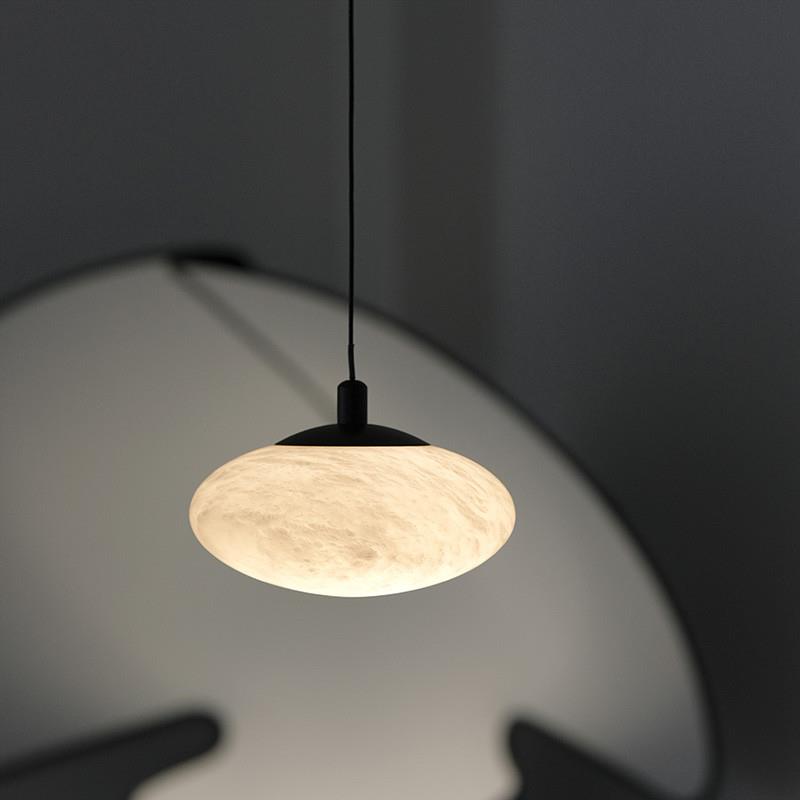 Clérachic Mini Discus pendant light lit in front of a large dark round mirror, warm stone against cool grey.