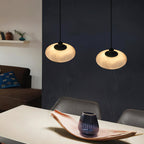 A pair of Clérachic Mini Discus pendant lights over a dining table on a deep navy wall, warm light on the tabletop.